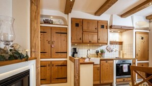 A kitchen with wooden cabinets, a stove, and a dining area with a chair. - Kehlstein - Reich Family (Schoenau am Koenigssee)