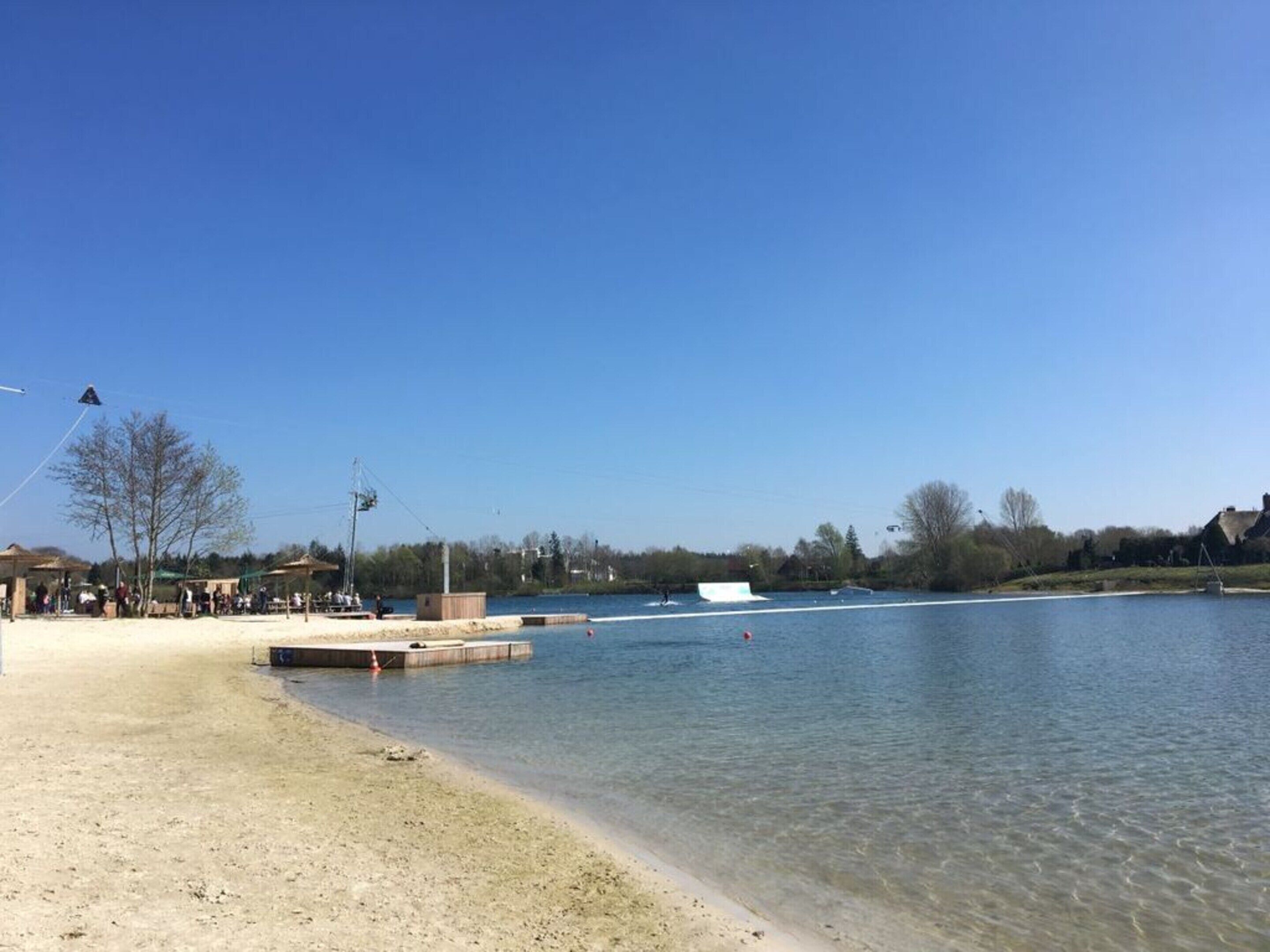 A lakeside area with a sandy beach, a dock, and a small building.