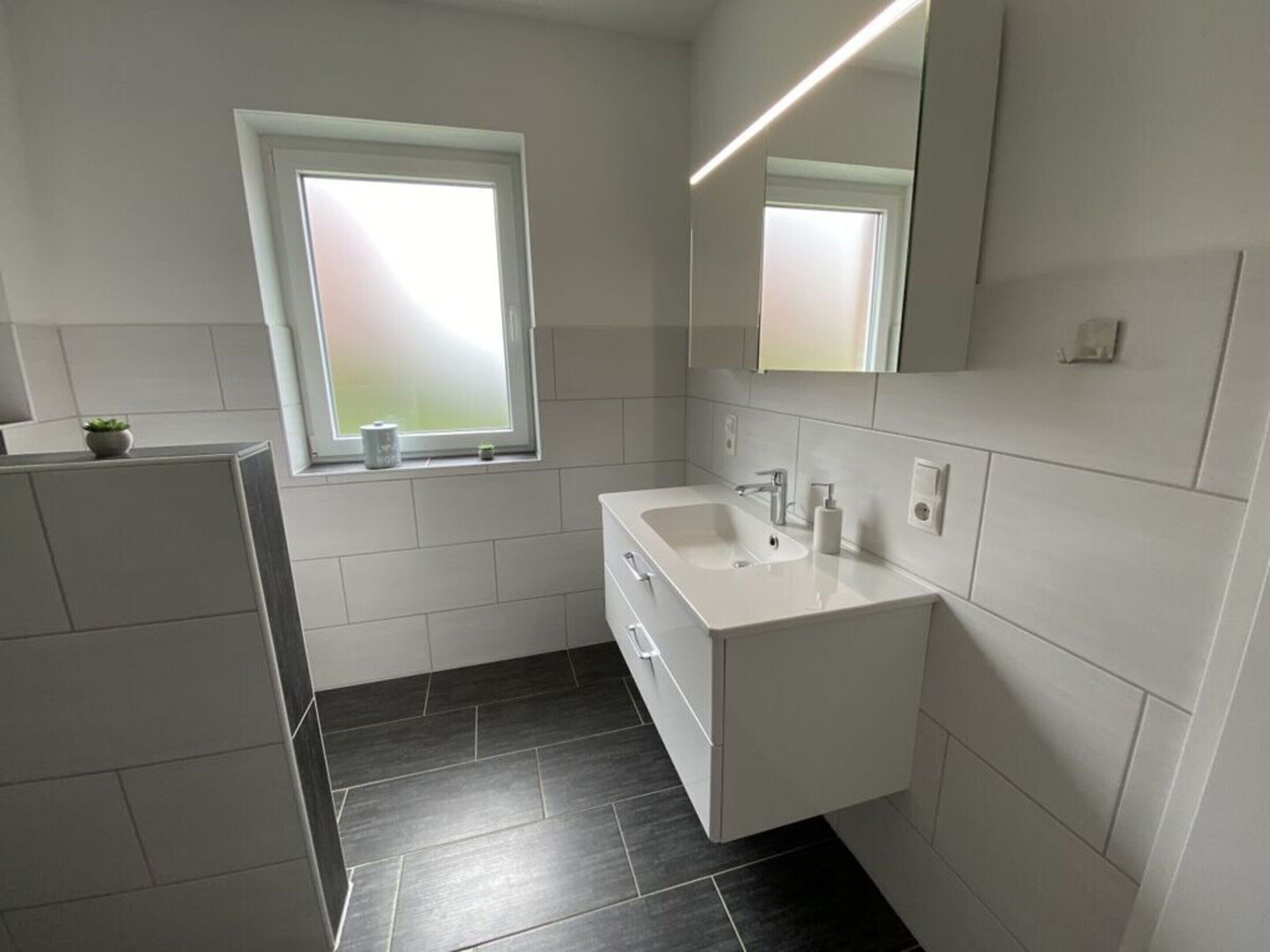 Un bagno moderno con un mobile lavabo bianco, uno specchio grande e una finestra.