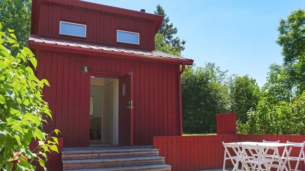 Un edificio di legno rosso con un portone d'ingresso, gradini che conducono alla porta e un piccolo portico con mobili da esterno bianchi.