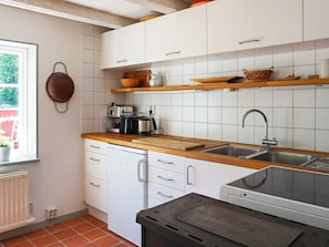 Une cuisine avec des meubles blancs, un plan de travail en bois, un évier et une fenêtre donnant sur un espace verdoyant.