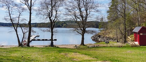 A lakeside view with a dock, trees, and a red building.