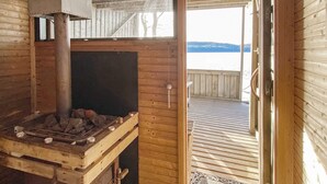 A wooden cabin with a fireplace, a door leading to a deck, and a view of a body of water.
