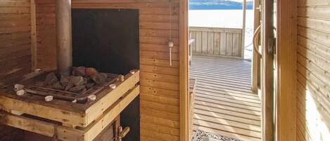 Una cabaña de madera con chimenea, una puerta que da a una terraza y vistas a un cuerpo de agua.