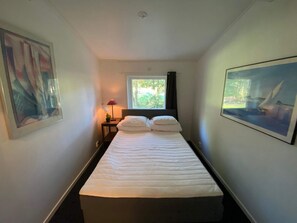 Une chambre d’hôtel avec un lit, une fenêtre donnant sur un paysage verdoyant, une table de chevet avec une lampe et un tableau encadré au mur.