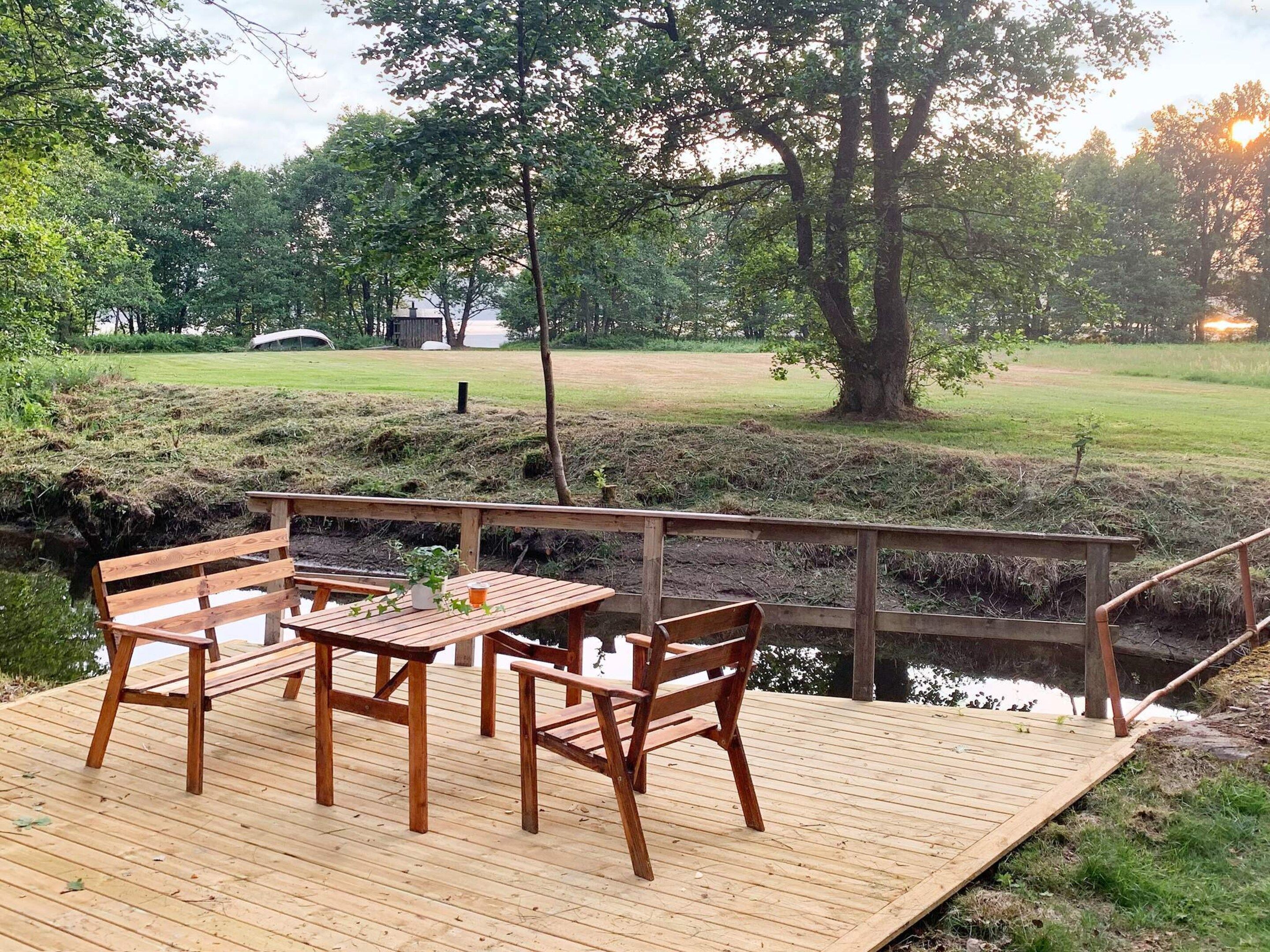 Une terrasse en bois, dotée de bancs et d’une table, qui offre une vue sur une zone herbeuse et une étendue d’eau.