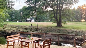 A wooden deck with benches and a table, overlooking a grassy area and a body of water.