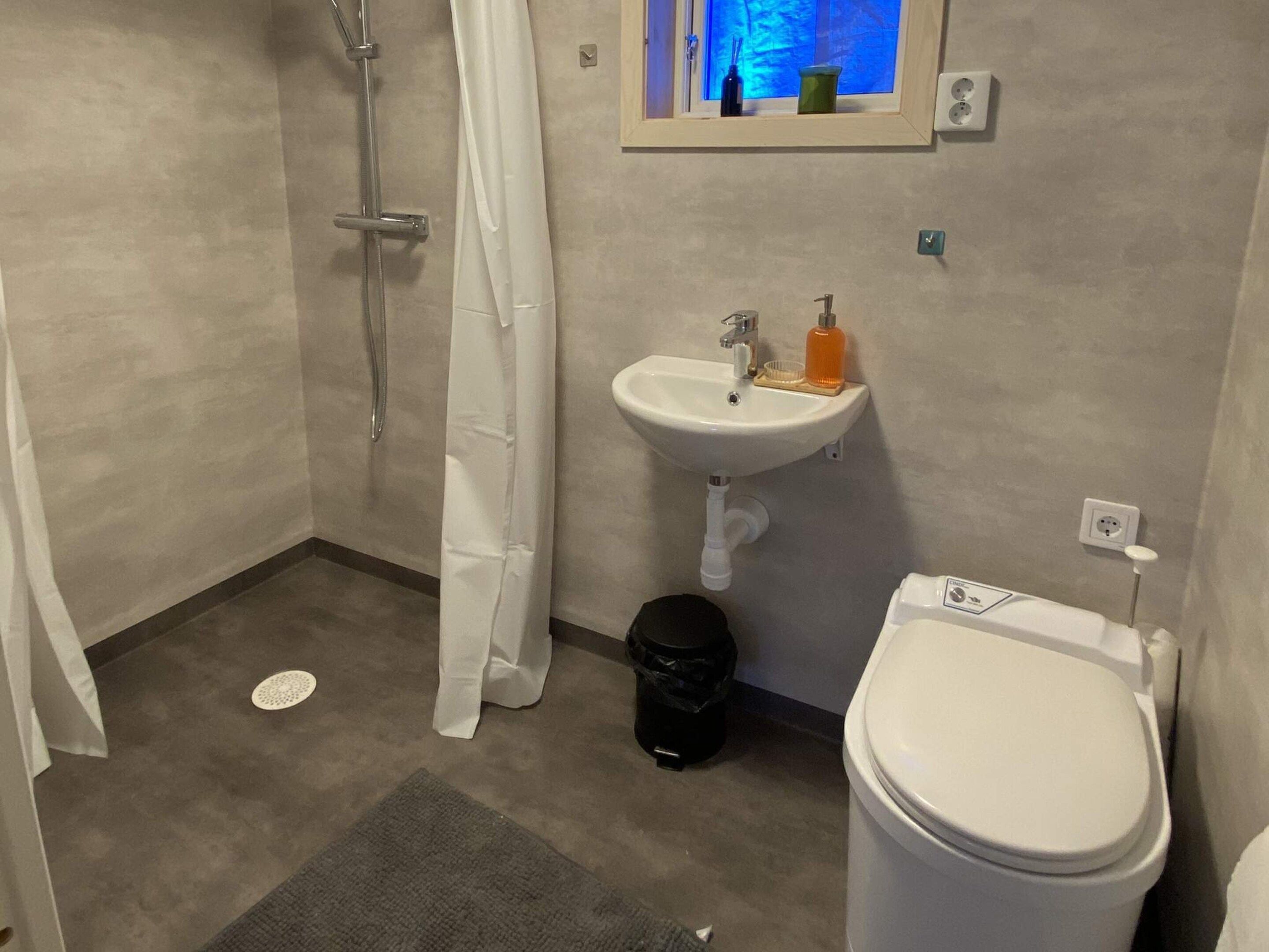 Et badeværelse med bruser, håndvask, toilet og et vindue med udsigt.