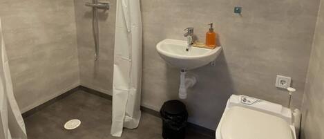Et badeværelse med bruser, håndvask, toilet og et vindue med udsigt.
