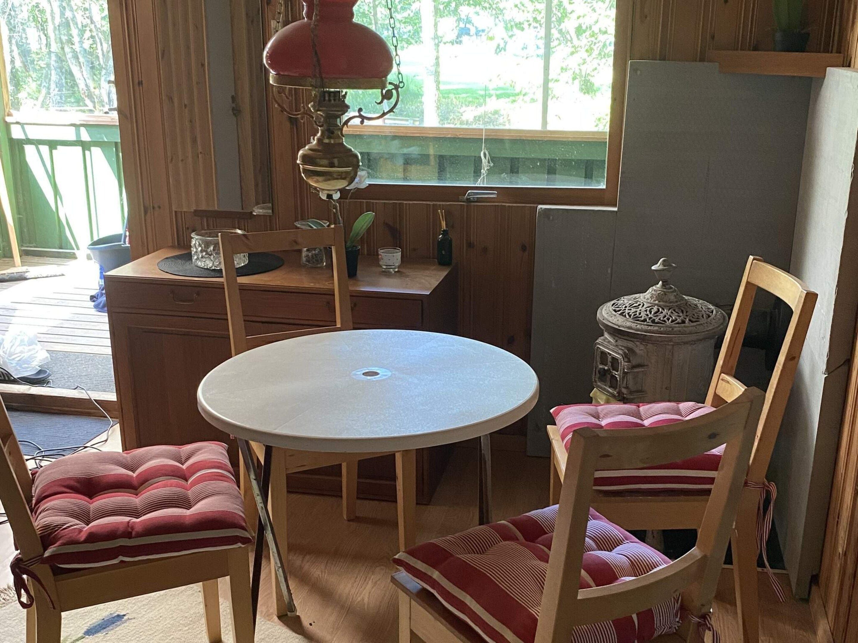 Un coin repas en bois avec une table ronde et deux chaises, une fenêtre donnant sur un paysage verdoyant et un poêle décoratif.