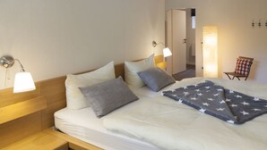 Ein ordentlich bezogenes Bett mit weißer Decke und Kissen, einem Holzkopfende und einem Nachttisch mit Lampe.