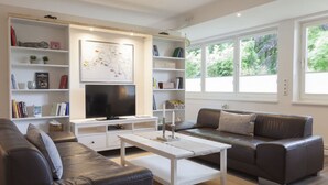 Ein modernes Wohnzimmer mit einer Couch, Couchtisch, Fernseher und Bücherregalen.