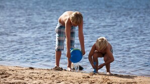 Twee personen op een strand, met een rustige zee op de achtergrond.