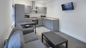 A modern apartment with a kitchenette, a sofa, a dining table, and a TV mounted on the wall. - Apartment 4 in Loftus (Saltburn-by-the-Sea)