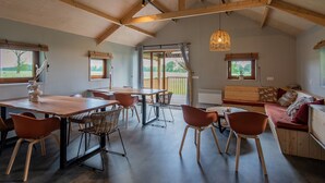 A spacious room with a high ceiling, wooden beams, a dining area with a table and chairs, a sofa, and a view through a glass door to an outdoor area. - Lodge in Drenthe With Scenic Veranda (Ruinerwold)
