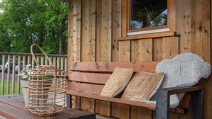 A wooden bench with woven cushions and a basket with flowers on a wooden deck. - Lodge in Drenthe With Scenic Veranda (Ruinerwold)