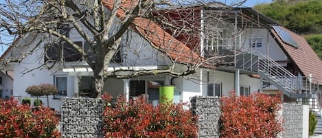 A two-story house with a red-tiled roof, a staircase, and a metal fence with red foliage.