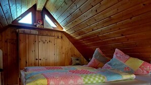 A cozy attic bedroom with a wooden sloped ceiling, a bed with colorful quilts, and a skylight. - Eisenmann Holiday Farm (Gengenbach)