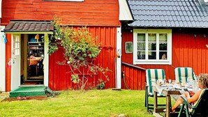A red wooden house with a tiled roof, a front door, and a small garden area with two chairs and a table. - 4 Person Holiday Home in Solvesborg-by Traum (Sölvesborg)