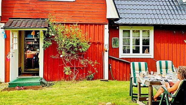 A red wooden house with a tiled roof, a front door, and a small garden area with two chairs and a table. - 4 Person Holiday Home in Solvesborg-by Traum (Sölvesborg)