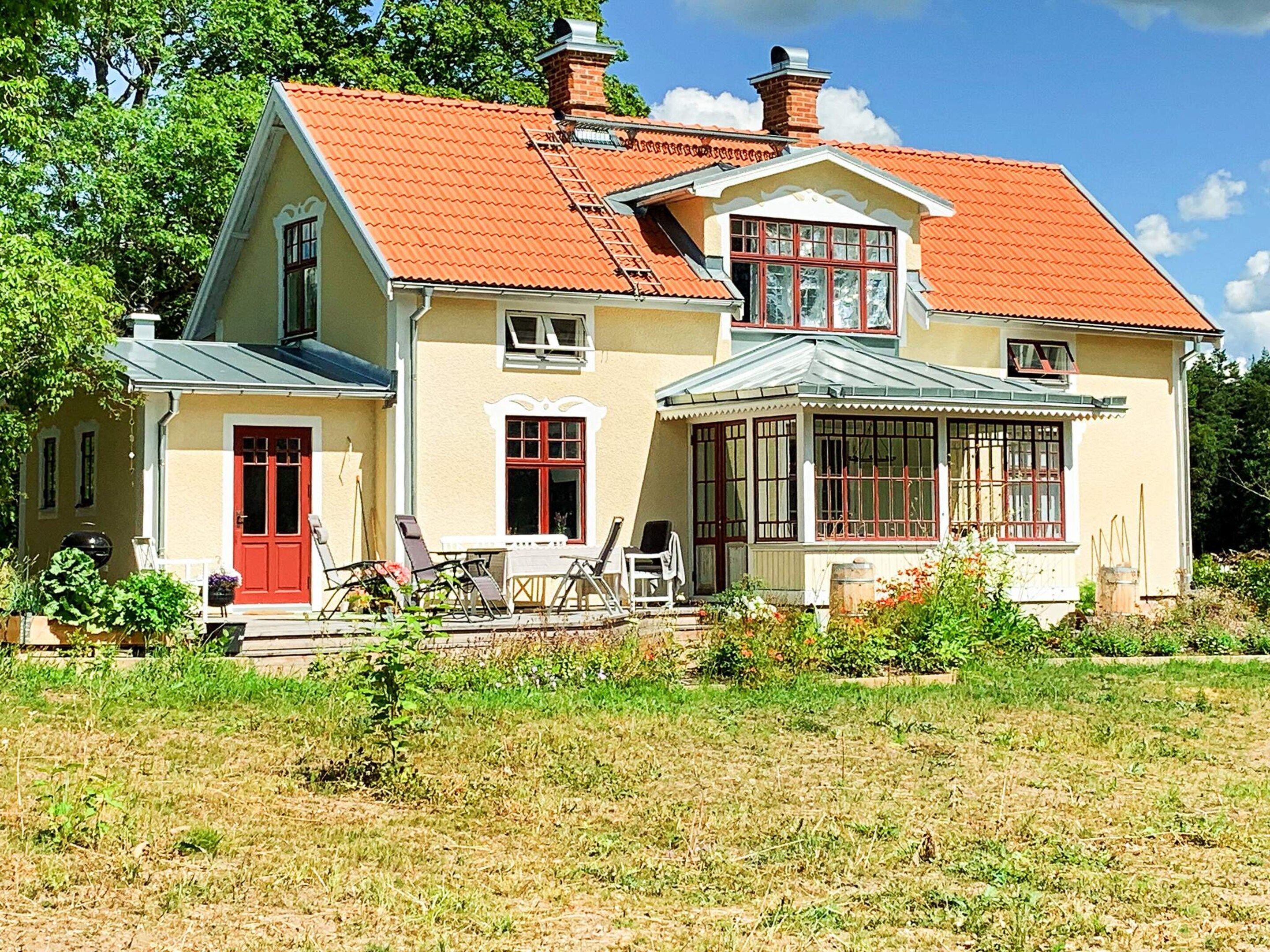 Une maison à deux étages avec un toit rouge, une véranda et un jardin.