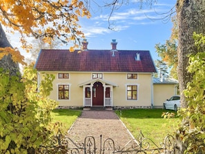 Une maison à deux étages, avec un toit recouvert de tuiles rouges, une entrée centrale dotée d’un porche blanc et une allée gravillonnée.