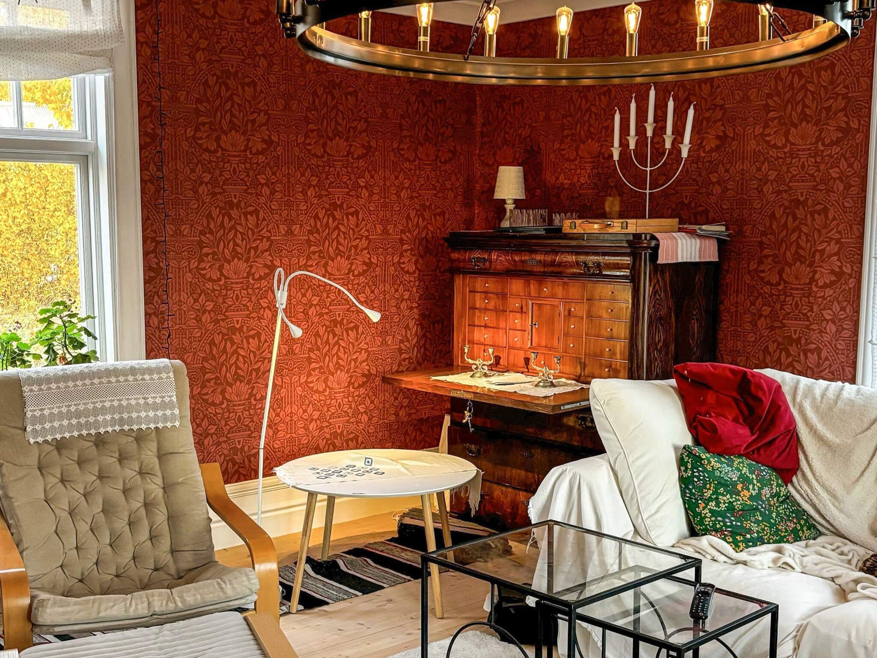 A cozy living room with a red patterned wallpaper, a wooden cabinet, a glass coffee table, and a comfortable sofa.