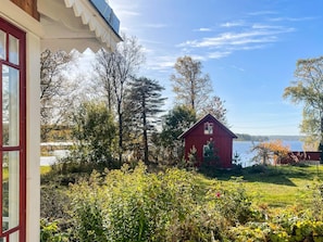 A red wooden house with a gabled roof, surrounded by lush greenery and trees, with a body of water in the background. - 5 Star Holiday Home in Bello (Hjältevad)