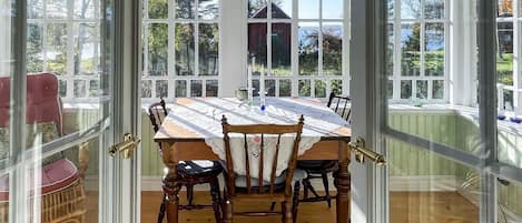 A dining area with a wooden table and chairs, large windows, and a view of a house and trees.