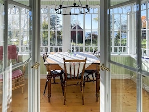 Un coin repas avec une table et des chaises en bois, de grandes fenêtres et une vue sur une maison et des arbres.
