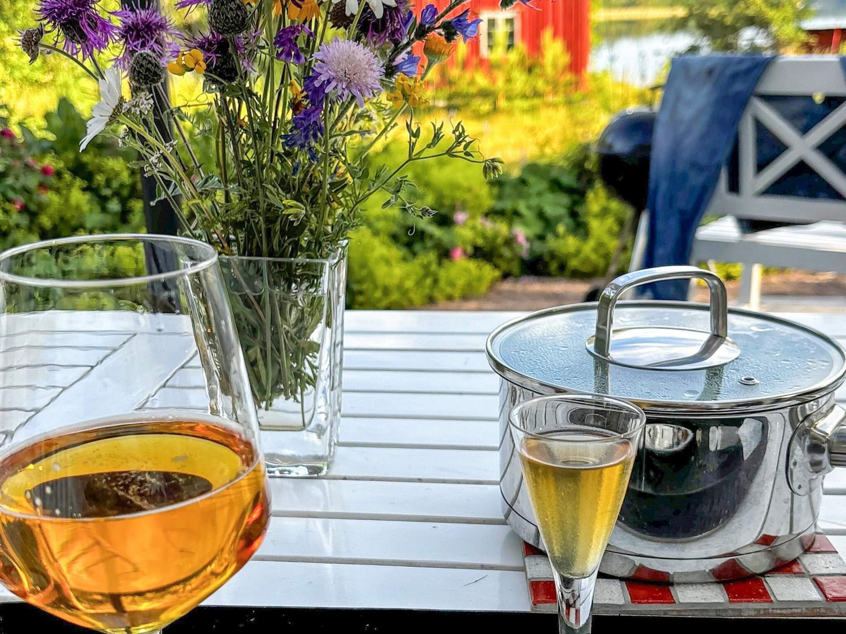 A table with a glass of beer, a glass of white wine, a pot, and a vase with flowers.