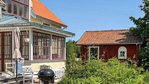 Een huis met een overdekte patio, een barbecue en een tuin vol rode bloemen.