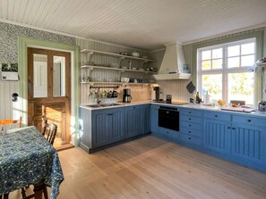 Une cuisine avec des meubles de rangement bleus, une table à manger en bois et une fenêtre avec des rideaux.
