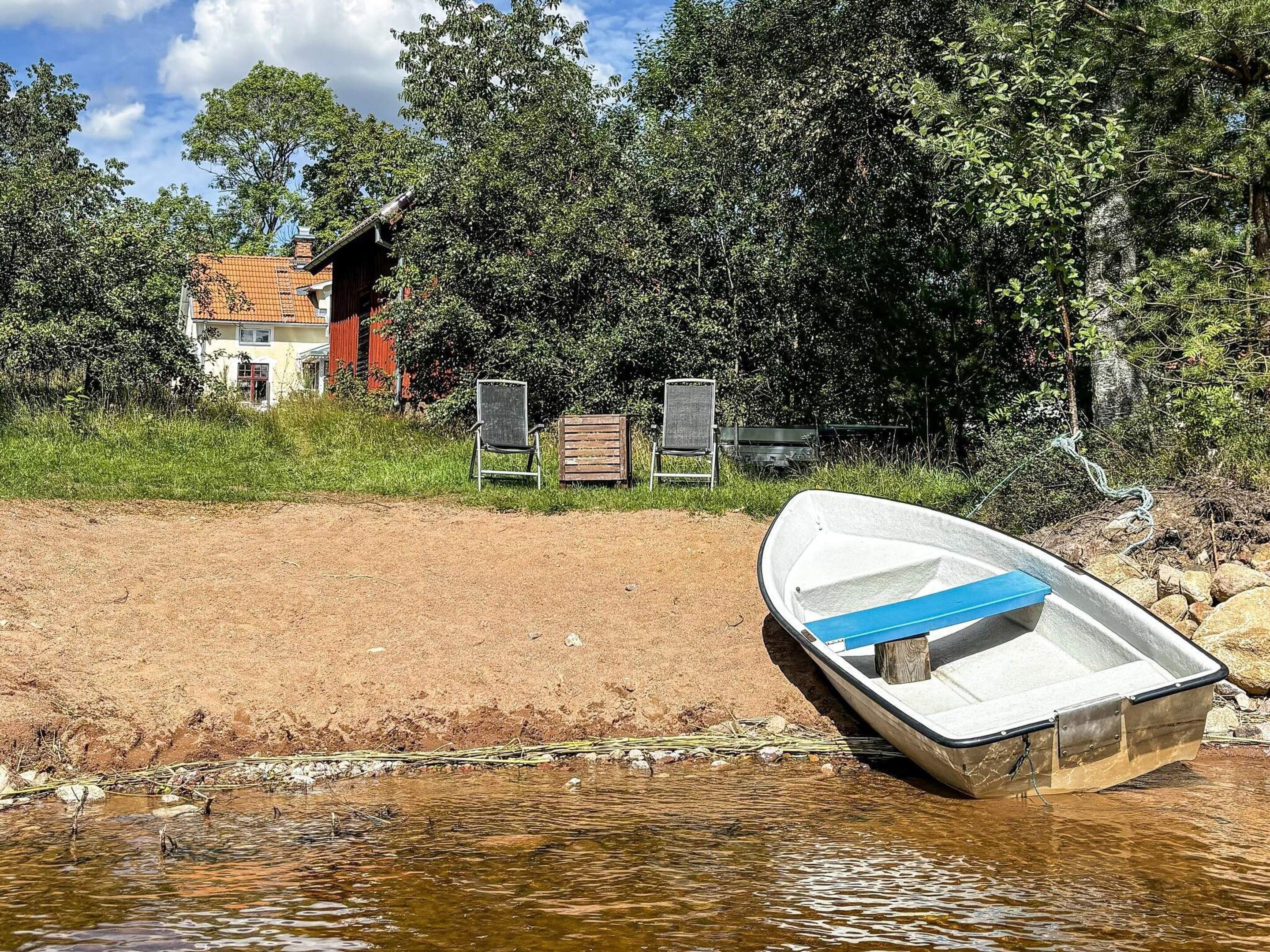 A boat on a sandy shore with a house and chairs in the background.