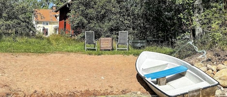 A boat on a sandy shore with a house and chairs in the background.