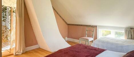 A bedroom with two beds, a wooden floor, a window with curtains, and a chair.