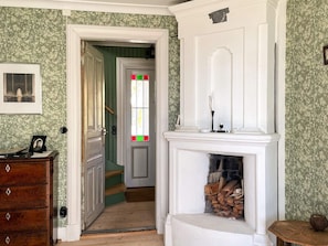 Un couloir avec une commode en bois, une cheminée surmontée d’une étagère, et une porte donnant sur une autre pièce.