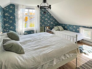 Une chambre avec un grand lit, un plus petit lit, une fenêtre avec des rideaux, un radiateur et un lustre.