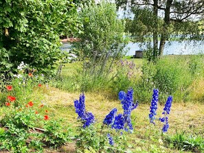 A garden with various plants and flowers, a body of water in the background, and a building with a red roof. - 5 Star Holiday Home in Bello (Hjältevad)