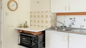 Een keuken met een oude fornuis, een gootsteen en een klok aan de muur.