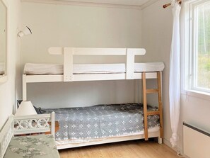 A bunk bed room with a window, a radiator, and a small table with a lamp.
