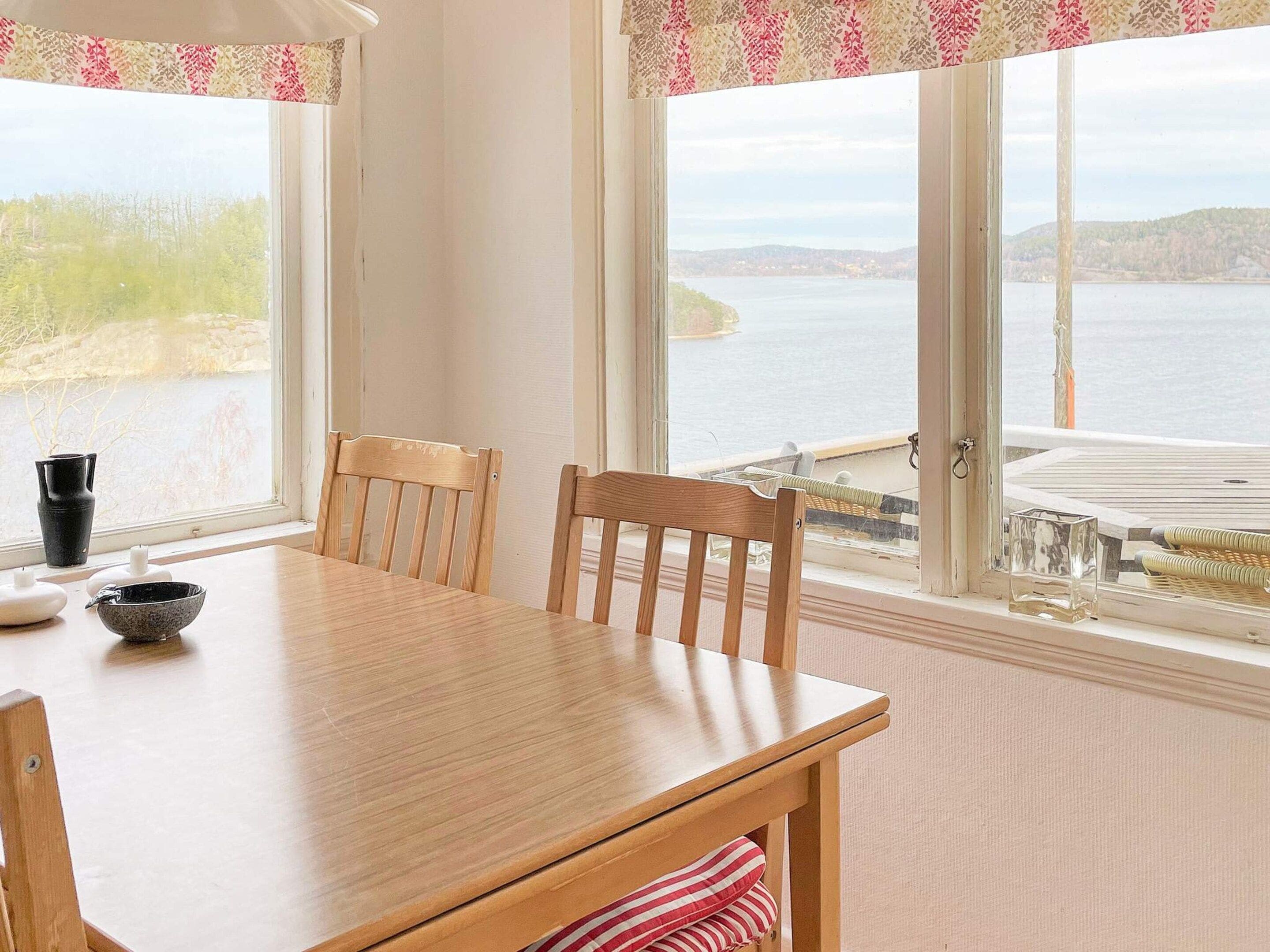 A wooden dining table with two chairs, a vase, and a bowl on the windowsill.
