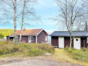 A rustic cabin with a red roof, surrounded by trees and a gravel path.