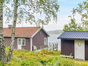 En stuga vid sjön med en brygga, omgiven av träd och växtlighet.