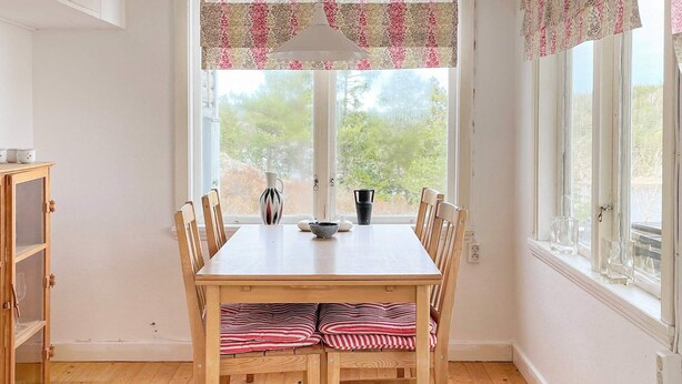 Een eetgedeelte met een houten tafel, stoelen en een raam met uitzicht op bomen.
