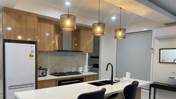 Une cuisine moderne dotée d’un îlot central, de tabourets de bar, d’un four encastré et de luminaires suspendus.