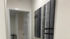 Un couloir doté d’un plancher en bois, une porte donnant sur une autre pièce et une œuvre d’art abstraite accrochée au mur.