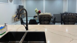 Un salon moderne avec une table à manger en verre, deux canapés, un baby-foot et un téléviseur fixé au mur.