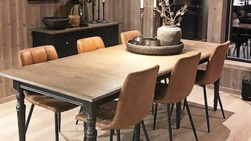 Ein Essbereich mit einem langen Tisch, sechs Stühlen, einer Vase mit Zweigen und einem Kerzenständer.