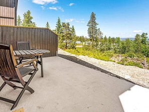 A patio with a wooden table and chairs, a concrete floor, and a view of a forest and distant buildings. - 7 Person Holiday Home in Lampeland (Flesberg)